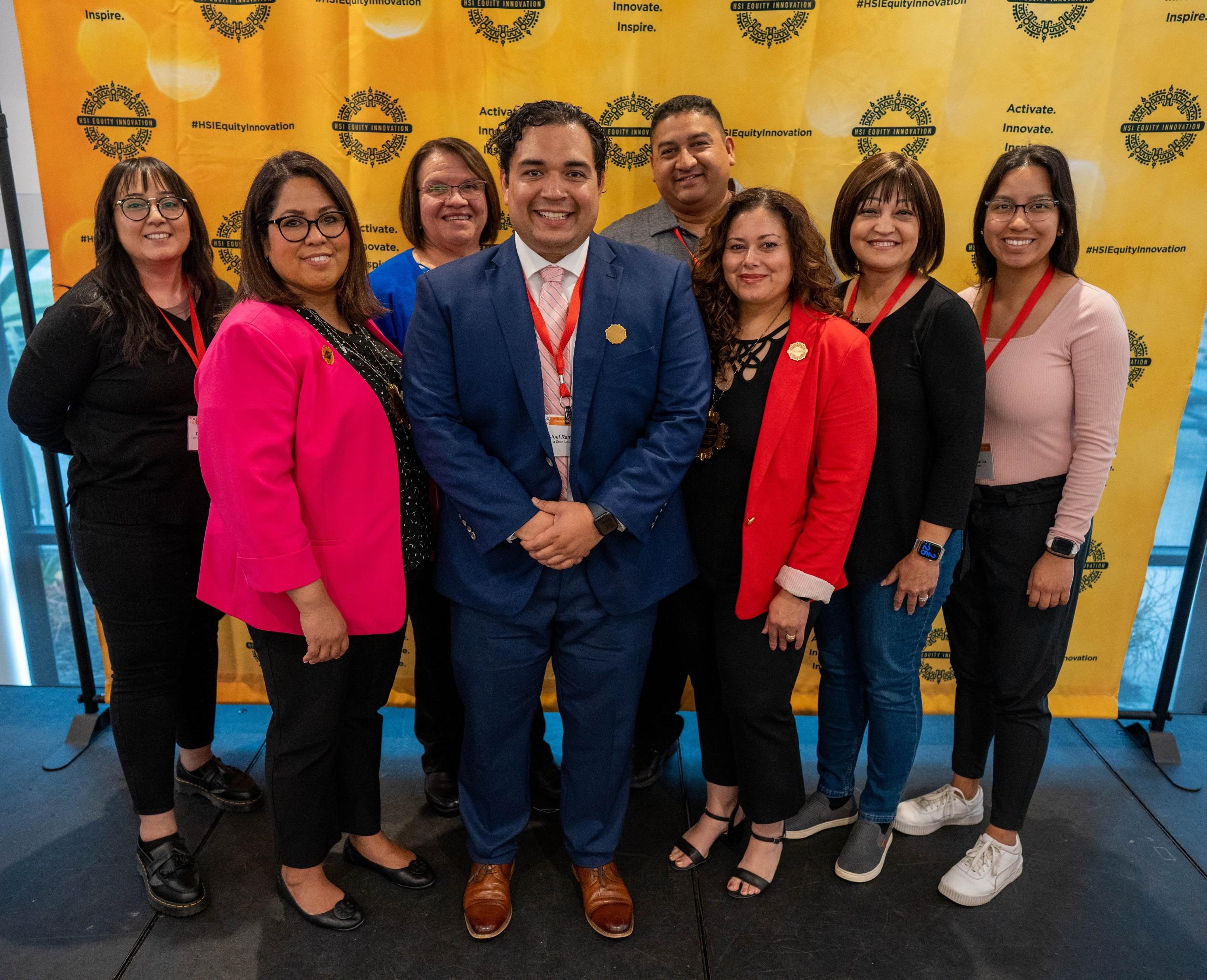 Eight Hub team members smiling in front of an HSI Equity Innovation step-and-repeat banner.